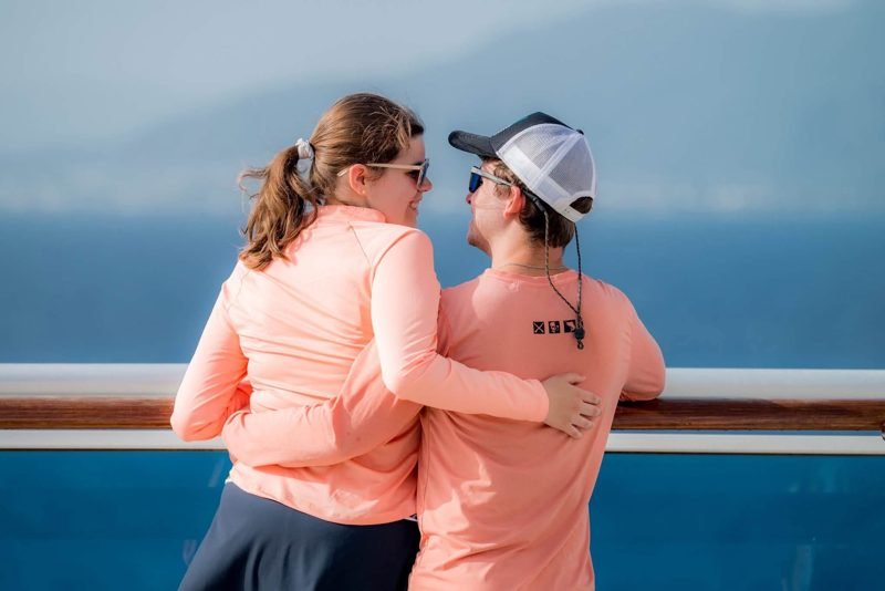 The couple from behind at a ship's rail, arms around each other, looking out to sea.