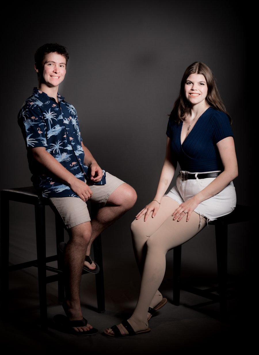 The couple seated on stools in a studio portrait, both smiling.